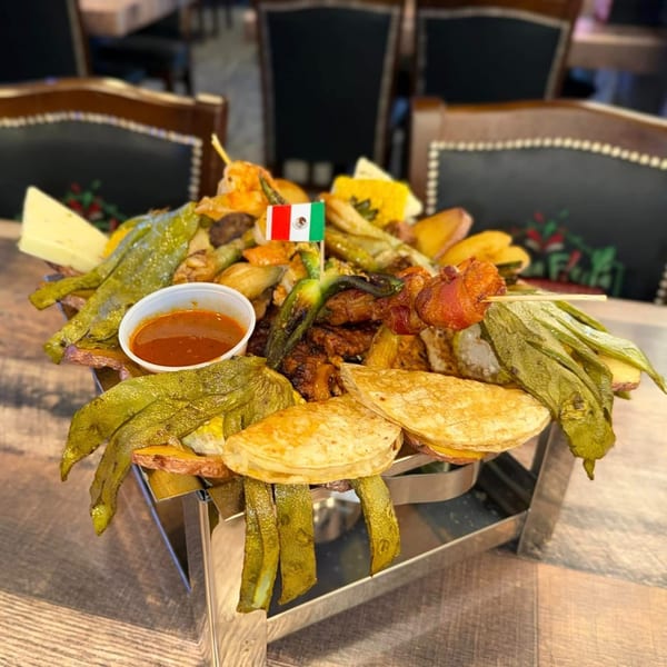 A large platter of grilled meats, vegetables, and quesadillas with a Mexican flag toothpick.