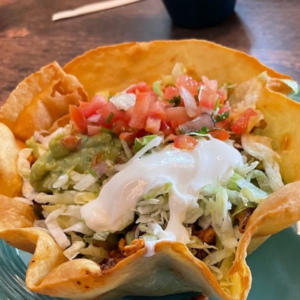 A taco salad in a crispy tortilla bowl, topped with guacamole, sour cream, lettuce, and pico de gallo.