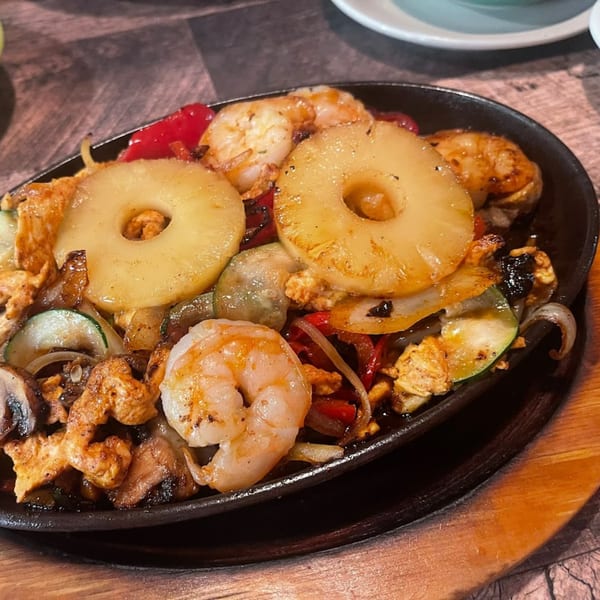 Sizzling fajitas with chicken, shrimp, pineapple, and vegetables in a black skillet at La Plaza Fiesta.