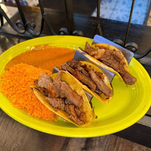 Three steak tacos with melted cheese, orange rice, and a side of red sauce on a bright yellow plate.