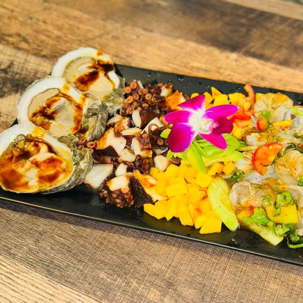 A black platter with oysters, octopus, mango, and shrimp ceviche, garnished with a purple orchid.