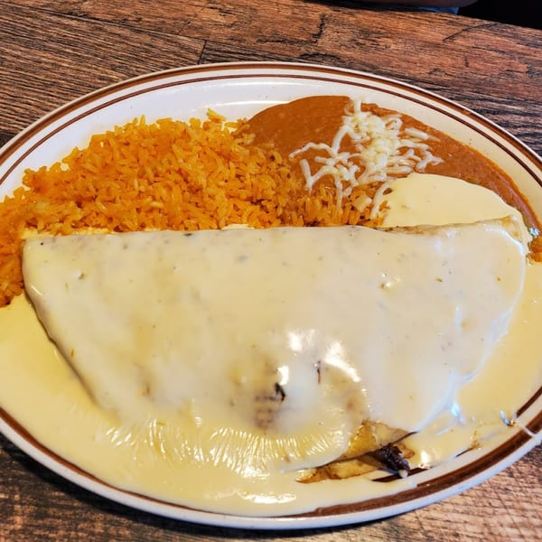 A Mexican dish with a large quesadilla covered in white cheese sauce, rice, and refried beans.