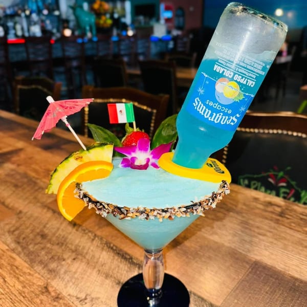 A blue margarita with a Seagram's Escapes bottle inverted, garnished with fruit and a Mexican flag.